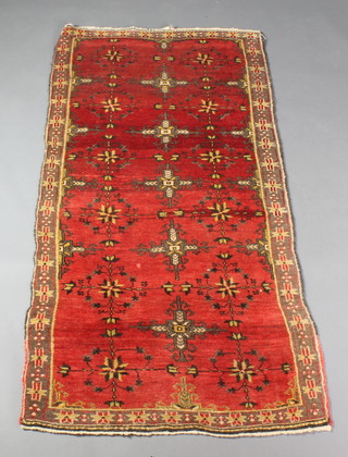 A red ground Persian rug with 5 stylised hooks to the centre with floral ground 77" x 38" 