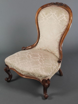 A Victorian carved walnut show frame nursing chair upholstered in cream sculptured dralon, raised on cabriole supports