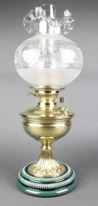 A Victorian brass oil lamp raised on a green ceramic base with clear chimney and etched glass shade