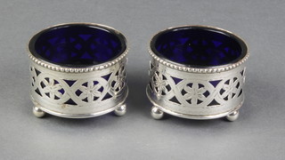 A pair of Edwardian pierced silver circular table salts on ball feet with blue glass liners, Birmingham 1902 