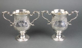 A pair of 18th Century Irish silver twin handled cups with floral repousse decoration and chased armorials by Matthew West, 28 ozs 