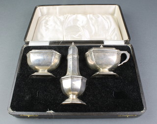 An Art Deco 3 piece panelled silver condiment set comprising a waisted table salt with blue glass liner, a pepperette and a waisted mustard pot with blue glass liner, Birmingham 1932, 220 grams