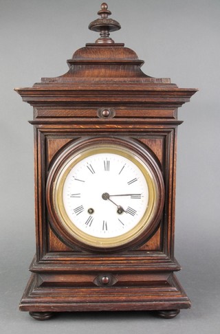 A striking bracket clock with enamelled dial and Roman numerals contained in an oak case surmounted by a lidded urn 