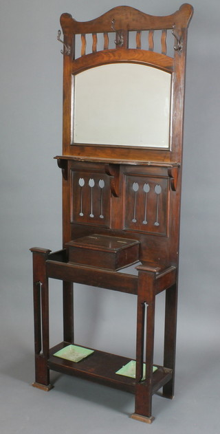 In the manner of Charles Voysey, an Arts and Crafts oak hall stand, the raised back with arched plate mirror, the base fitted a glove box and having stylised tulip decoration, complete with drip trays 83"h x 30"w x 12"d 