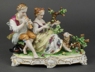 An early 20th Century German porcelain fete galant group of a couple sitting beside a tree with a lamb at their feet, on a rococo base 10" 