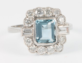 An 18ct white gold aquamarine and diamond ring, the centre emerald cut stone surrounded by 12 brilliant and 2 baguette cut diamonds, size P