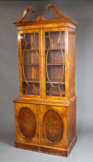 A Georgian style figured walnut bookcase on cabinet, the upper section with pierced broken pediment, fitted adjustable shelves enclosed by astragal glazed doors, the base fitted a cupboard enclosed by a pair of oval panelled doors, raised on a platform base 91"h x 36 1/2"w x 24"d 