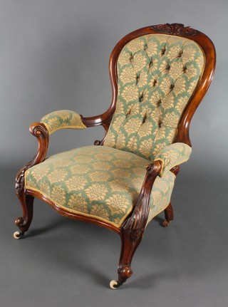 A Victorian carved mahogany open arm chair, the seat and back upholstered in green buttoned material, raised on cabriole supports 
