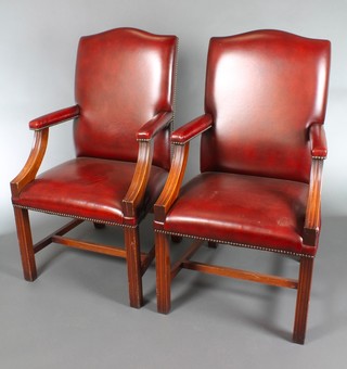 A pair of mahogany framed library chairs, the seats and backs upholstered in red leather material, raised on square tapering supports with H framed stretcher 