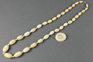 A string of oval ivory beads, a carved bone brooch