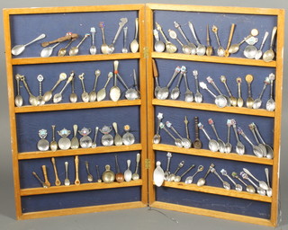 A quantity of mainly silver plated souvenir spoons in a hinged hanging wall cupboard