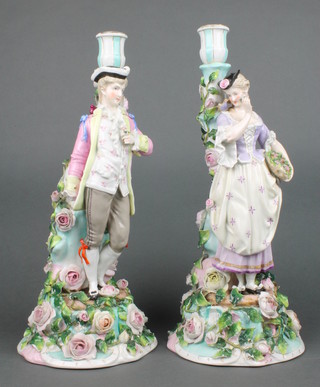A pair of late 19th Century German porcelain candlesticks in the form of a standing lady and gentleman, the base applied with flowers 15" 
