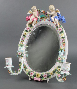 A late 19th Century German porcelain oval wall mirror the crests mounted by 2 cherubs, the frame with applied flowers and swing sconces 13" 