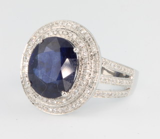 A 14ct white gold oval cut sapphire and diamond ring, the centre stone approx 6.75ct surrounded by  2 tiers of brilliant cut diamonds with brilliant cut diamond shoulders, size M 