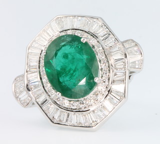 An 18ct white gold emerald and diamond cluster dress ring, the centre stone approx. 9.1ct surrounded by tapered baguettes and brilliant cut diamonds approx. 2.8ct, size O 