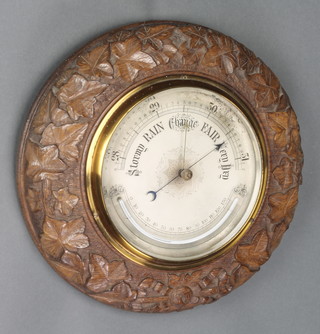 An aneroid barometer and thermometer with silvered dial contained in an carved oak case with leaf decoration 12" 