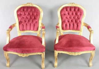 A pair of gilt painted open arm salon chairs upholstered in red buttoned material on cabriole supports 