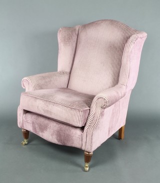 A Georgian style winged armchair upholstered in striped purple material, raised on turned supports with brass caps 