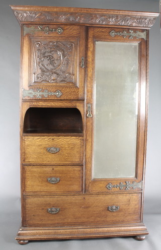 An Arts & Crafts carved oak combination wardrobe with moulded cornice fitted a cupboard enclosed by a panelled door decorated a stylised dragon above a recess above 2 short drawers and 1 long drawer flanked by a cupboard enclosed by a bevelled plate mirror panelled door, the base fitted a drawer, raised on bun feet 77 1/2"h x 48"w x 21"d 