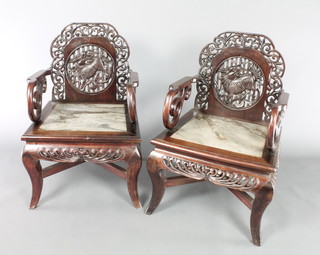A pair of pierced Chinese carved hardwood dining chairs, the backs decorate dragons and with white veined seats, raised on cabriole supports