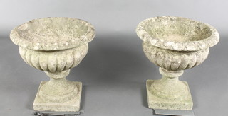 A pair of well weathered circular composition garden urns with lobed borders, raised on square feet 18" x 19" diam. 