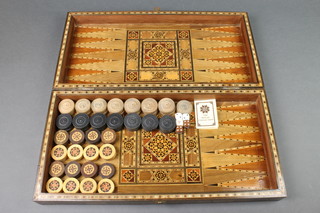 A Middle Eastern parquetry games compendium inlaid a chessboard and backgammon board with hinged lid, the interior with 16 black and white counters together with 15 associated black and white counters 3"h x 19" x 10" when closed x 19" when open 