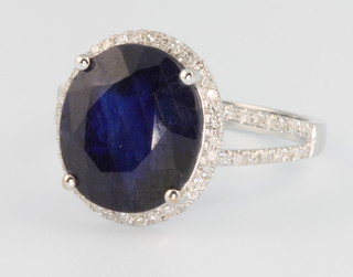 A 14ct white gold sapphire and diamond oval ring, the centre stone approx. 7.25ct surrounded by brilliant cut diamonds on an open shank 0.4ct, size M 1/2 