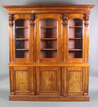 A Victorian mahogany triple bookcase on cabinet the upper section with moulded cornice, fitted adjustable shelves enclosed by arched panelled doors with vitruvian scrolls to the base, the base fitted triple cupboards enclosed by panelled doors and raised on a platform base 83"h x 77 1/2"w x 14" (made up) 