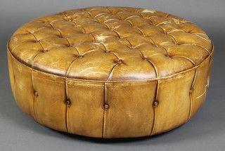 A circular footstool upholstered in buttoned tan leather 12"h x 36"diam. 
