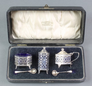 A silver 3 piece hexagonal condiment set with pierced decoration and blue glass liners, together with a spoon Birmingham 1918, 64 grams