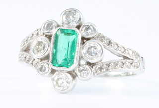 An 18ct white gold emerald and diamond cluster ring, the centre emerald approx 0.5ct, size M 