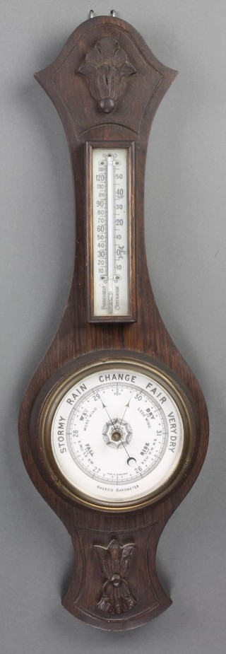 An aneroid barometer and thermometer with porcelain dial contained in a carved oak wheel case 