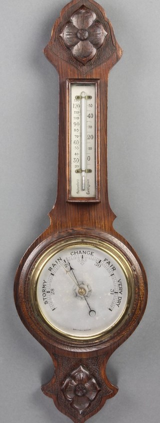 An aneroid barometer and thermometer with silvered dial, contained in a carved oak wheel case 