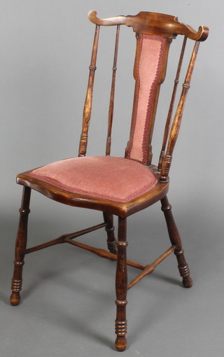 An Edwardian mahogany stick and rail back bedroom chair upholstered in pink Dralon, raised on turned supports with H framed stretcher 