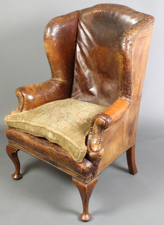 An 18th Century walnut winged armchair upholstered in original brown leather with brass studs,  raised on cabriole supports 