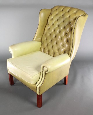 A Georgian style winged armchair upholstered in buttoned green leather