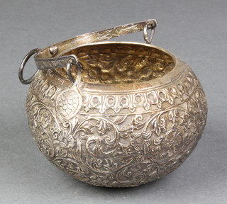 A repousse Indian silver bowl with swing handle decorated with scrolls