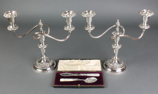 A cased pair of silver plated spoon and knife with mother of pearl handles and a pair of plated 2 light candelabra 