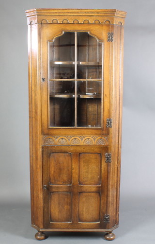 An "Ipswich" style oak double corner cabinet, the upper section with carved and moulded cornice, the interior fitted shelves enclosed by glazed panelled doors, the base enclosed by a panelled door, raised on bun feet 71 1/2"h x 30"w x 18"d 