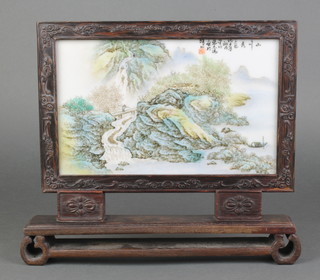 An early 20th Century Chinese table screen with painted porcelain panel depicting an extensive landscape with a man crossing a bridge with script in a carved hardwood frame 10" x 11 1/2"