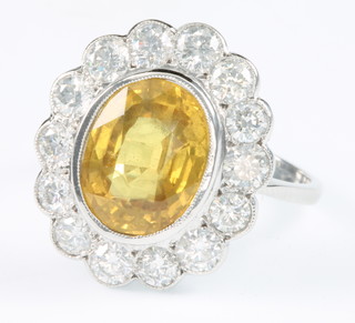A white gold oval yellow sapphire and diamond ring, the centre stone approx 4.5ct surrounded by 14 brilliant cut diamonds approx. 1.4ct, size O