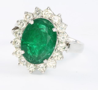 A 14ct white gold emerald and diamond oval cluster ring the centre stone surrounded by 16 brilliant cut diamonds 0.8ct size 0 1/2