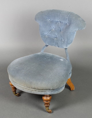 A Victorian metal framed nursing chair upholstered in blue buttoned material, raised on turned supports ending in brass caps and castors 