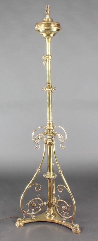 A Victorian brass adjustable standard oil lamp converted to electricity, raised on a triform base 