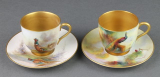 A pair of Royal Worcester coffee cups and saucers decorated with peacocks and pheasants, decorated by J Stinton