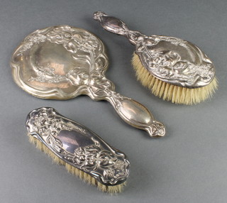 A silver Art Nouveau dressing table set comprising hand mirror, clothes brush and hair brush, the repousse decoration with flowers, Birmingham 1908/1915 