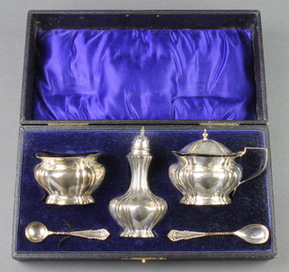 An Edwardian silver condiment set of baluster form comprising a mustard, salt and pepper together with 2 spoons, Birmingham 1908 and 1909, cased, 156 grams