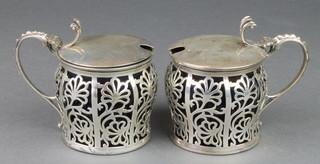 A pair of fancy silver mustards with pierced bulbous bodies, scroll handles and blue glass liners, Chester 1923, 310 grams