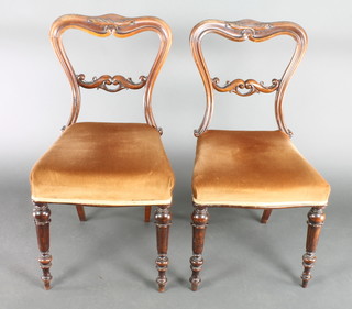 A pair of Victorian carved mahogany buckle back dining chairs with shaped mid rails, the seats upholstered in brown material, raised on turned and fluted supports 