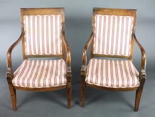 A pair of carved walnut Empire style open arm chairs upholstered in red and white striped material, raised on splayed supports